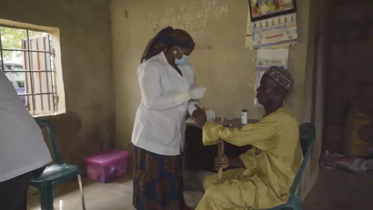 A clinician consulting with patients under a shelter during the Kano outreach.
